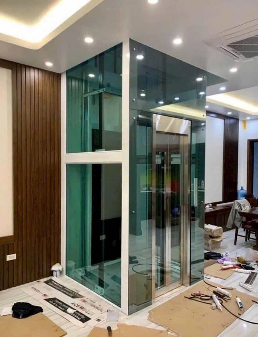 Thang máy kính gia đình nhỏ gọn đang lắp đặt trong phòng khách hiện đại